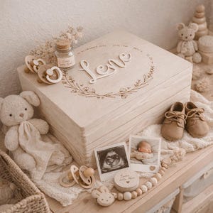 Könnte beinhalten: Eine hellfarbene Holz-Andenkenbox mit dem Namen "Lene" obenauf, umgeben von einem floralen Kranz. Die Box ist von Babyartikeln umgeben, darunter Schnuller, ein Teddybär, Babyschuhe und Ultraschallfotos. Die Box misst 30 cm.