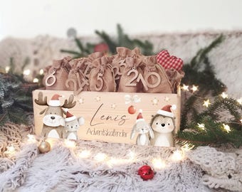 May include: A wooden Advent calendar with burlap sacks numbered 1-24. The calendar box features cartoon reindeer, koala, bunny, and hedgehog characters wearing Santa hats. The text "Lenis Adventskalender" is also on the box.