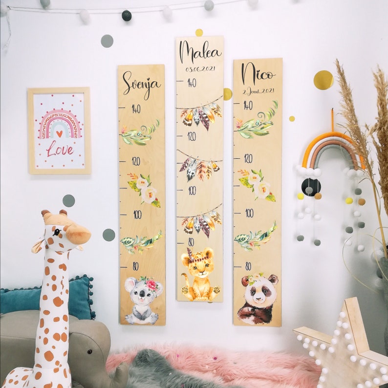 May include: Three wooden growth charts with animal illustrations and names. The charts are decorated with floral and feather designs. The names on the charts are Malea, Svenja, and Nico. The charts are marked with measurements in centimeters.