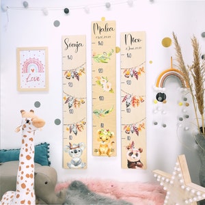 May include: Three wooden growth charts with a boho theme. Each chart features a different animal: a koala, a lion, and a panda. The charts are decorated with feathers, leaves, and flowers. The charts are labeled with the names "Svenja", "Malea", and "Nico" and their birth dates.