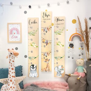 May include: Three wooden growth charts with animal illustrations and floral accents. The charts are labeled with the names "Carla", "Elisa", and "Alina" and their birth dates. The charts measure from 80 to 140 centimeters.