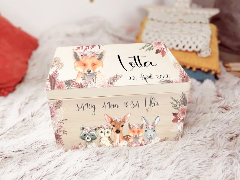 K&ouml;nnte beinhalten: Eine h&ouml;lzerne Erinnerungsbox mit einem Blumendesign, das einen Fuchs, ein Reh, eine Eule, einen Waschb&auml;r und ein Kaninchen zeigt. Die Box ist personalisiert mit dem Namen "Lotta", dem Datum "22. April 2022" und der Uhrzeit "16:34 Uhr". Die Box enth&auml;lt auch die Ma&szlig;e "3410g" und "49cm".