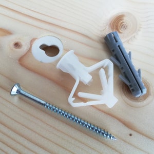 May include: A close-up of a white plastic drywall anchor, a silver screw, and a gray plastic wall anchor. The anchors are designed to be used with screws to secure objects to drywall.