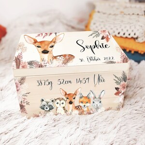 K&ouml;nnte beinhalten: Eine Holz-Erinnerungskiste mit einer hellen Holzoptik und einem floralen Design. Die Kiste hat einen Klappdeckel und ist mit einem Reh, einer Eule, einem Waschb&auml;r, einem Fuchs und einem Hasen verziert. Die Kiste ist personalisiert mit dem Namen "Sophie", dem Datum "30. Oktober 2022" und der Uhrzeit "14:51 Uhr". Die Kiste enth&auml;lt auch die Ma&szlig;e "3875g 52cm".