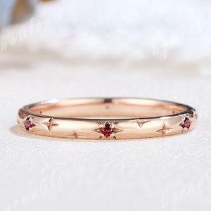 Könnte beinhalten: Ein dünner Roségoldring mit einem zarten Sternendesign und kleinen roten Edelsteinen, die entlang der Kante gesetzt sind.