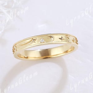 May include: A gold band ring with a delicate design of stars, moons, and a small diamond. The ring is a simple and elegant piece of jewelry.
