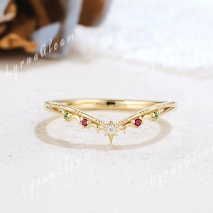 Puede incluir: Un anillo dorado con un diseño curvo. El anillo presenta un engaste central en forma de estrella con un pequeño diamante, flanqueado por piedras preciosas rojas y verdes. El anillo probablemente está hecho de oro y está diseñado para usarse en un dedo.