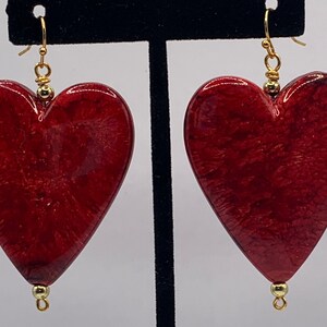 Puede incluir: Un par de pendientes de corazón rojo con detalles dorados. Los pendientes están hechos de un material texturizado que se asemeja a la madera.