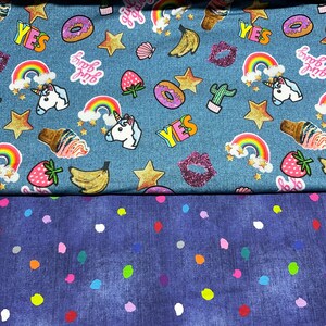 Könnte beinhalten: Blauer Jeansstoff mit einem bunten Muster aus Einhörnern, Regenbögen, Sternen, Bananen, Erdbeeren, Eiswaffeln, Donuts, Lippen und dem Wort "YES". Der Stoff ist mit einem zweiten Stück blauen Jeansstoff mit weißem Punkte-Muster kombiniert.