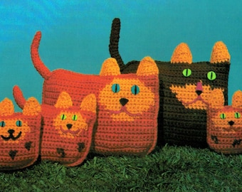 May include: Five crocheted cat toys in various sizes. The largest cat is orange and brown with green eyes. The other four cats are orange and brown with black eyes. The cats are sitting on a bed of green grass.