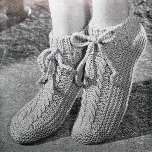 May include: A pair of gray knitted slipper socks with a cable knit pattern and a lace-up design. The slippers have a tassel detail at the top.