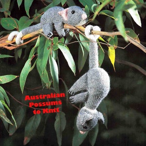 May include: Two grey knitted possums hanging from a tree branch. The text "Australian Possums to Knit" is printed below the possums.