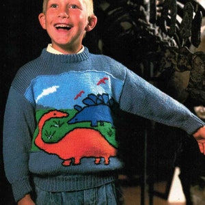 May include: A blue knitted sweater with a dinosaur design. The sweater features a red and orange dinosaur with a long neck and a blue dinosaur with a spiky back. The dinosaurs are on a green and blue background with white clouds.