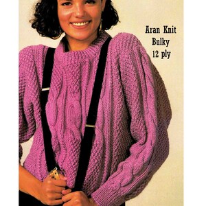 Könnte beinhalten: Ein rosa Aran-Strickpullover mit einem Zopfmuster. Der Pullover hat schwarze Träger und ist aus dickem 12-fädigem Garn gefertigt.