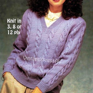 May include: A light purple cable-knit sweater with a V-neck. The sweater has a textured design and is worn over a white collared shirt. The text "Knit in 3, 8 or 12 ply" is visible in the upper left corner.