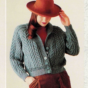 May include: A teal blue cable knit cardigan with a button closure. The cardigan has a collar and long sleeves. The model is wearing a red turtleneck underneath and a brown corduroy skirt.