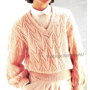 May include: A pink knitted sweater with a V-neck and a lacy pattern. The sweater has long sleeves and a ribbed hem.