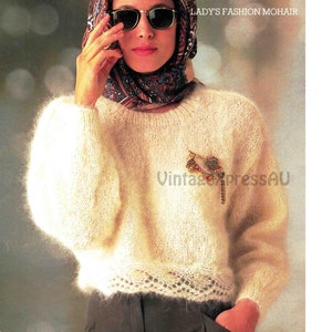 Könnte beinhalten: Ein weißer Mohairpullover mit einer zarten Spitzenborte am Saum. Der Pullover hat einen runden Ausschnitt und lange Ärmel. Eine dekorative Brosche ist an der Vorderseite des Pullovers befestigt.