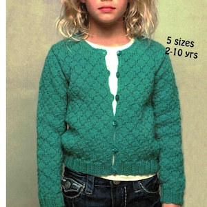 Puede incluir: Un cárdigan verde turquesa con estampado de rombos y cierres de botones. El suéter se usa sobre una camisa blanca y se combina con jeans azules. El texto de la imagen dice "5 tallas 2-10 años".
