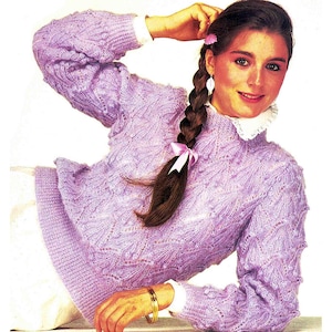 May include: A lavender knitted jumper with a delicate lace pattern. The jumper has a high neckline and long sleeves.