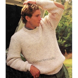 Puede incluir: Un suéter de punto de color crema con textura de canalé. El suéter tiene cuello redondo y mangas largas. El suéter tiene un parche en el codo.