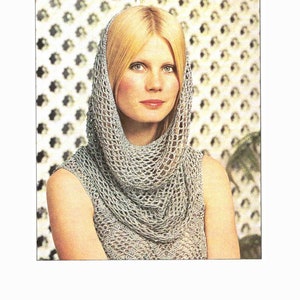 Może przedstawiać: Kobieta w jasnoszarej szydełkowej chuście i kapturze. Chusta opada na ramiona i klatkę piersiową, a kaptur otacza twarz. Wzór szydełkowy wydaje się otwarty i przewiewny, tworząc delikatną fakturę. Tło to biało-zielony wzór.