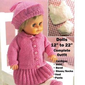 May include: A doll wearing a complete pink knitted outfit, including a cardigan, skirt, beret, shoes/socks, vest, and pants. The outfit is designed for dolls 12 to 22 inches in size. The doll is sitting on a white chair.