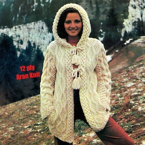 Könnte beinhalten: Ein weißer Kapuzenpullover mit einem Zopfmuster und Quastenbändern. Der Pullover ist aus 12-fädigem Aran-Strick gefertigt.