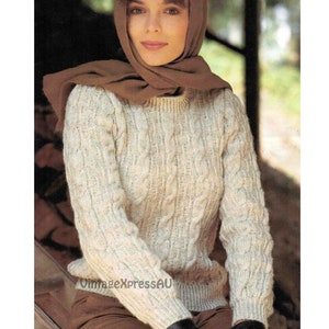 Puede incluir: Un suéter blanco de punto de cable con una bufanda marrón. El suéter tiene un cuello redondo y mangas largas.