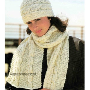 May include: A white knitted hat and scarf set with a cable knit pattern. The hat has a folded brim and the scarf is long and narrow.
