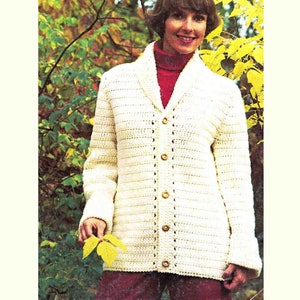 May include: A white crocheted cardigan with a shawl collar and button closure. The cardigan is shown being worn by a person in a fall setting.