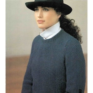 Puede incluir: Un suéter de punto azul oscuro con cuello redondo. El suéter lo lleva una persona con una camisa blanca de cuello debajo y un sombrero negro.