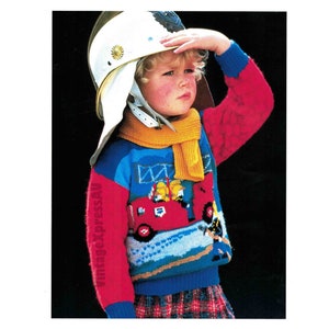 May include: A young child wearing a red, blue and yellow sweater with a fire engine design. The child is also wearing a white helmet and a yellow scarf.