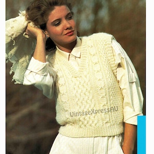 May include: A white knitted sleeveless sweater with a cable knit pattern. The sweater has a V-neck and is worn over a white button-down shirt.