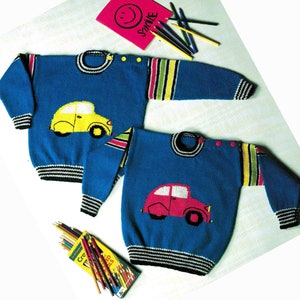 Könnte beinhalten: Zwei blaue Strickpullover mit langärmeligen, mehrfarbig gestreiften Mustern, schwarz-weiß gerippten Bündchen und einem Autodesign auf der Vorderseite. Ein Pullover zeigt ein gelbes Auto, der andere ein rosa Auto. Beide haben Knopfverschlüsse am Halsausschnitt.