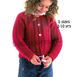 Op de afbeelding: Een rode gebreide cardigan met witte knopen. De cardigan heeft een textuurpatroon en wordt gedragen met een blauwe spijkerbroek. De tekst op de afbeelding luidt "5 maten 2-10 jaar".