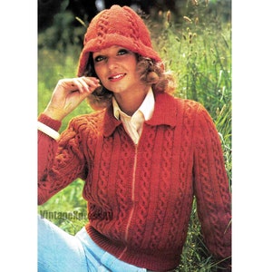 May include: A red knitted cardigan with a zipper closure and a cable knit pattern. The cardigan has a collar and long sleeves. The model is wearing a red knitted hat.