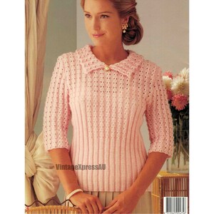 Puede incluir: Un suéter de punto rosa con un cuello ancho y un botón de perla. El suéter tiene un delicado patrón de calado y es de punto de canalé.