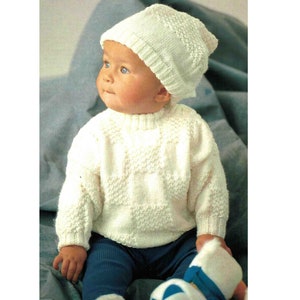 Może przedstawiać: Biały dzianinowy zestaw dla niemowlęcia składający się z swetra i czapki z fakturowanym wzorem. Sweter ma okrągły dekolt i długie rękawy. Czapka jest w stylu beanie.