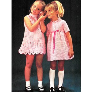 Könnte beinhalten: Zwei Mädchen tragen rosa gehäkelte Kleider. Das Kleid links hat einen hohen Kragen und ist ärmellos. Das Kleid rechts hat einen Kragen, kurze Ärmel und ein rosa Band, das in der Taille gebunden ist.