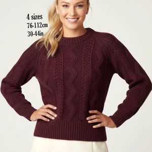 Pode incluir: Uma camisola de manga comprida e gola redonda num tom bordeaux profundo com um padrão de malha trançada vertical. A peça está disponível em 4 tamanhos, variando de 76 a 112 cm. A camisola tem punhos, bainha e gola canelados.