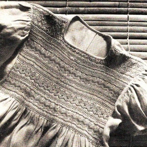 May include: A close-up of a white garment with a detailed embroidered neckline. The embroidery is done in a variety of stitches, creating a textured and intricate design.