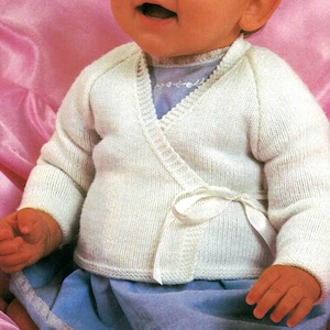 May include: A white knitted baby cardigan with a wrap-around style and a white satin ribbon tie. The cardigan is made of a soft, lightweight yarn and has a delicate, feminine design.