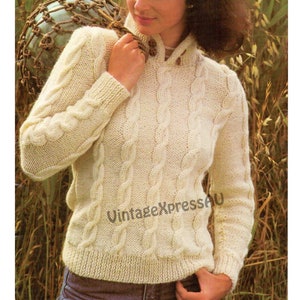 Könnte beinhalten: Ein weißer Strickpullover mit Zopfmuster, hohem Kragen und langen Ärmeln. Der Pullover hat ein schlichtes Design mit einem sich wiederholenden Zopfmuster.