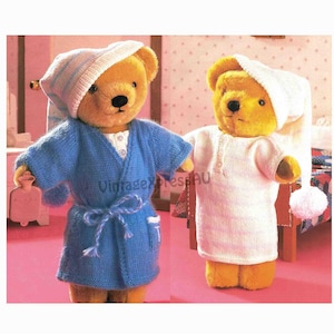 Puede incluir: Dos osos de peluche con pijamas de punto. Un oso lleva una bata azul con ribete blanco y un gorro de dormir a rayas blancas y azules. El otro oso lleva un camisón a rayas blancas y azules y un gorro de dormir blanco con un pompón blanco.