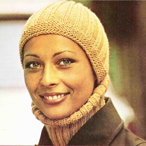 May include: A woman wearing a knitted hat and turtleneck in a warm, light brown color. The hat has a ribbed design, and the turtleneck is a matching color. The woman is smiling, and the background is blurred.