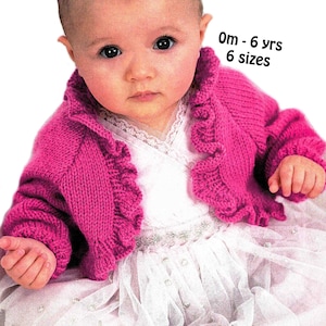 May include: A baby wearing a bright pink knitted cardigan with a ruffled collar and sleeves. The baby is also wearing a white dress with a tulle skirt. Text in the image reads "0m - 6 yrs 6 sizes".