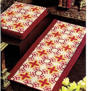 Może przedstawiać: Czerwono-biały dywan z geometrycznym wzorem krzyży i kół. Dywan jest wykonany z przędzy i ma czerwoną obwódkę. Dywan leży na drewnianej podłodze.