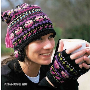 May include: A black knit hat with a pink and purple geometric pattern and a pink tassel. The hat has ear flaps and is worn by a person holding a white mug.
