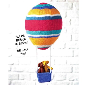 Puede incluir: Un globo aerostático de punto con un patrón de rayas en rojo, amarillo, azul y blanco. El globo tiene una cesta azul con dos ositos de peluche pequeños dentro. El texto "Hot Air Balloon & Basket DK 8 ply Knit" está impreso debajo del globo.